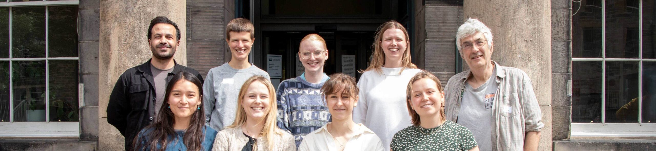 A group of university students standing formally in front of the entrance to Edinburgh Climate Change Institute